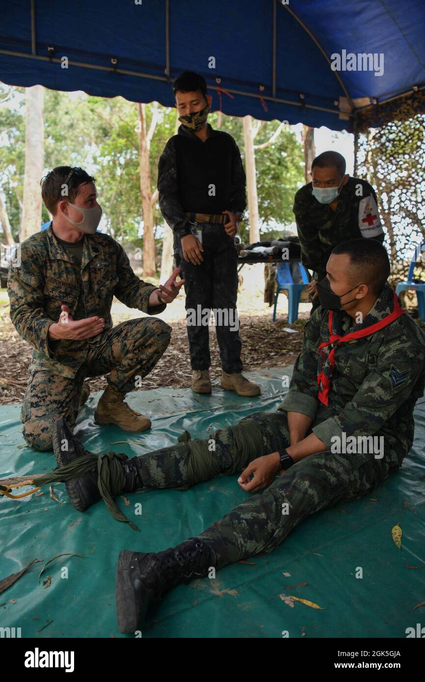 U.S. Navy Petty Officer 1st Class Philip Tockweiler, a corpsman with Headquarters and Support Company, 9th Engineer Support Battalion, 3rd Marine Logistics Group, with the help of a translator, explains to Royal Thai Army medical personnel how to build and apply an improvised emergency traction splint using materials in the environment during Exercise Cobra Gold 21 at Ta Mor Roi training area in Surin Province, Thailand, August 7, 2021. Royal Thai and American Armed Forces worked together during the exercise to conduct landmine disposal operations, render-safe procedure training, and partnered Stock Photo