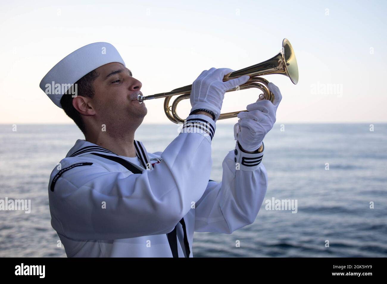 210808-N-EG940-3351 ATLANTIC OCEAN (Aug. 8, 2021) Aviation Boatswain's Mate (Fuel) 3rd Class Luis Marcano plays Taps during a burial at sea aboard the Wasp-class amphibious assault ship USS Kearsarge (LHD 3) Aug. 8, 2021. Kearsarge is underway to support Large-Scale Exercise (LSE) 2021. LSE 2021 demonstrates the Navy's ability to employ precise, lethal, and overwhelming force globally across three naval component commands, five numbered fleets, and 17 time zones. LSE 2021 merges live and synthetic training capabilities to create an intense, robust training environment. It will connect high-fid Stock Photo