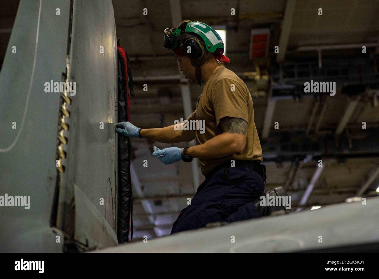 210809-N-DW158-1025 ARABIAN SEA (Aug. 9, 2021) – Aviation Structural Mechanic 3rd Class Nile Watson replaces screws on the wing of an F/A-18E Super Hornet fighter jet, attached to the “Dambusters” of Strike Fighter Squadron (VFA) 195, in the hangar bay of aircraft carrier USS Ronald Reagan (CVN 76) in the Arabian Sea, Aug. 9. Ronald Reagan is deployed to the U.S. 5th Fleet area of operations in support of naval operations to ensure maritime stability and security in the Central Region, connecting the Mediterranean and Pacific through the western Indian Ocean and three strategic choke points. Stock Photo