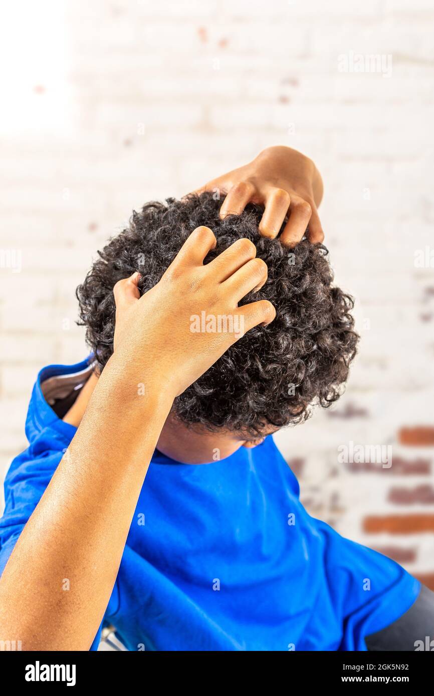 Smiling young boy scratching hair for head lice or allergies Stock