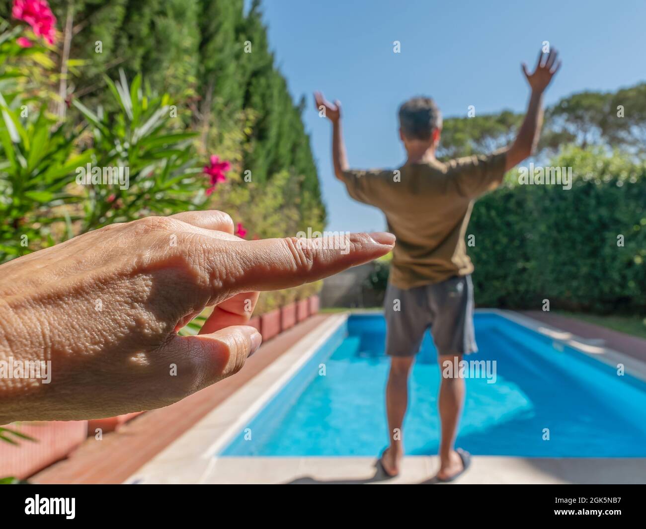 A female index finger seems to push a man into a swimming pool, for a game of perspective Stock Photo