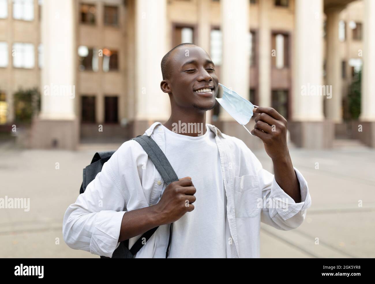 Happy black student guy taking off face mask, leaving university and ...