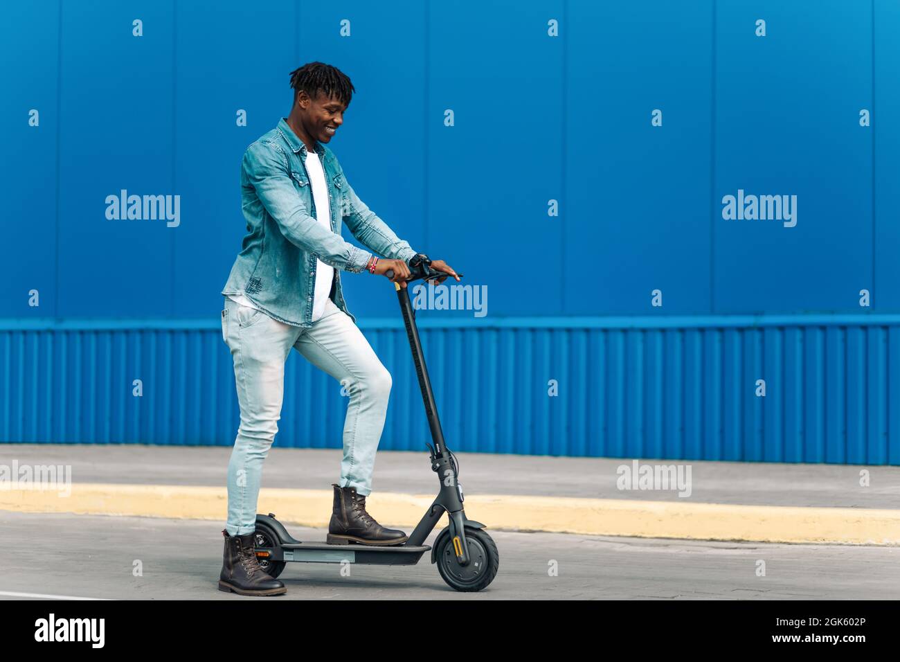 modern african american on electric scooter, business man is one to work, student is one to study, against the background of a blue building, side vie Stock Photo