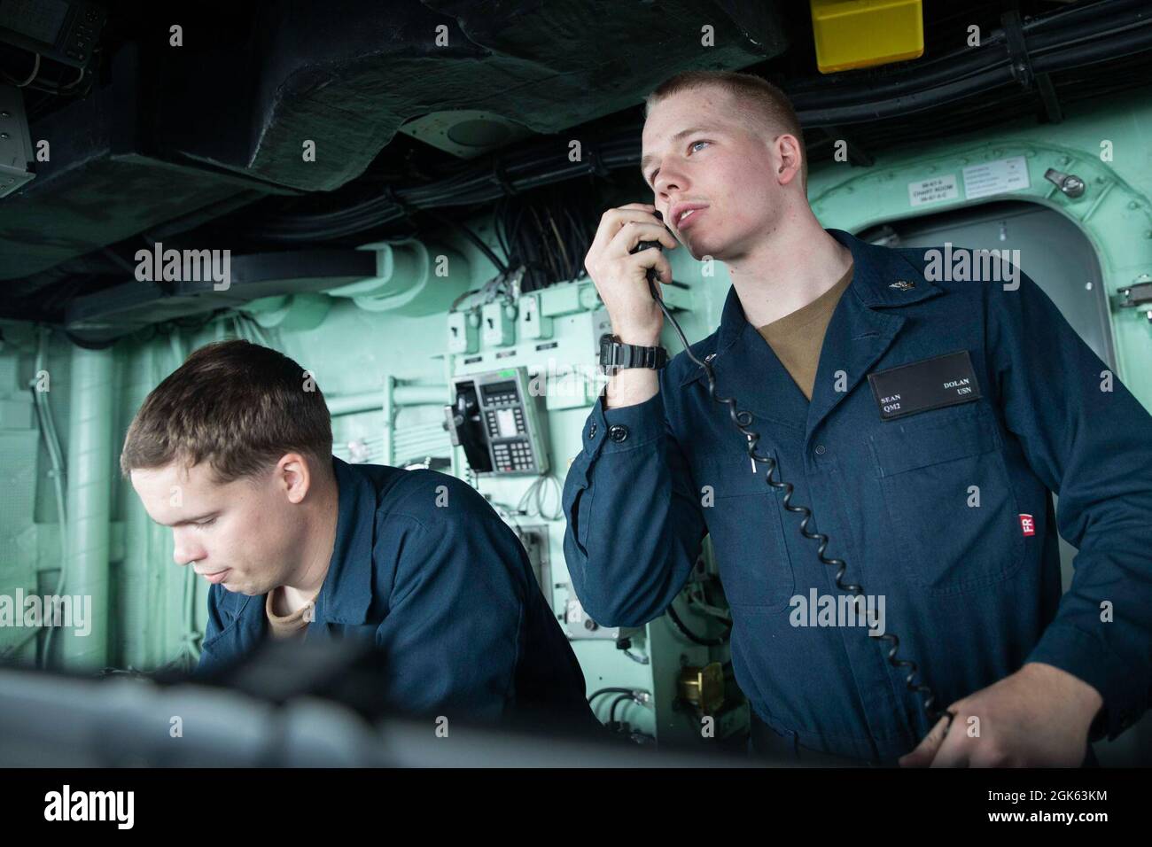 210812-N-OJ308-1019   GULF OF OMAN (Aug. 12, 2021) Quartermaster 2nd Class Sean Dolan, right, assigned to the Wasp-class amphibious assault ship USS Iwo Jima (LHD 7), delivers a message using the ship’s 1-MC as Quartermaster Seaman James Thompson makes a deck log entry, Aug. 12. Iwo Jima is deployed to the U.S. 5th Fleet area of operations in support of naval operations to ensure maritime stability and security in the Central Region, connecting the Mediterranean and Pacific through the western Indian Ocean and three strategic choke points. Stock Photo