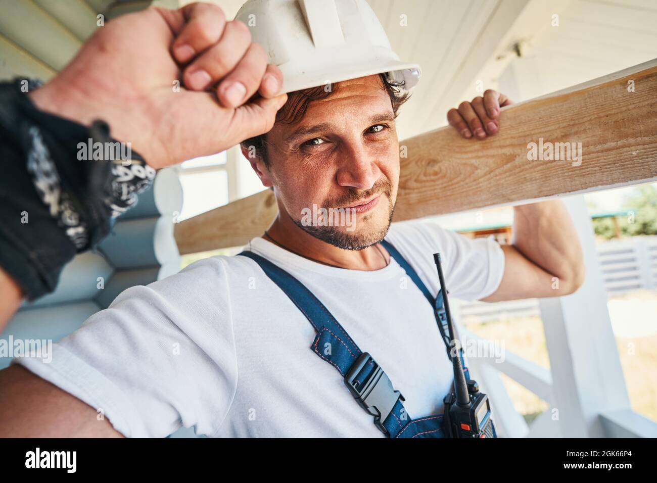 Hard-working builder adjusting his hard hat while carrying board Stock Photo