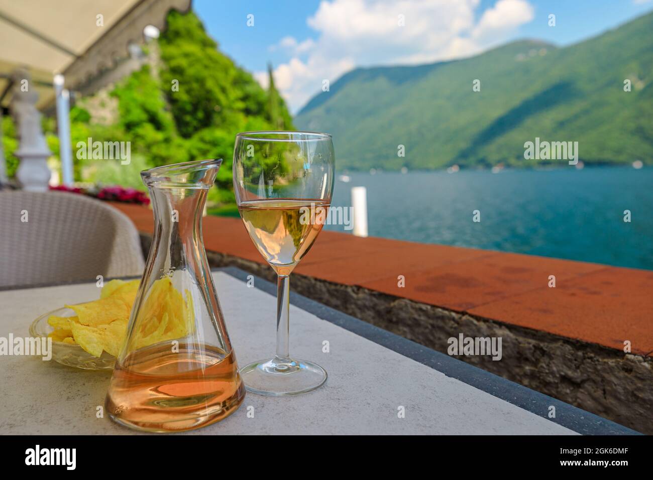 rose wine flute by the lakefront of Lugano city in Switzerland. Romantic appetizer in Ticino Canton on Swiss Lake Lugano of Switzerland. Olive trees Stock Photo