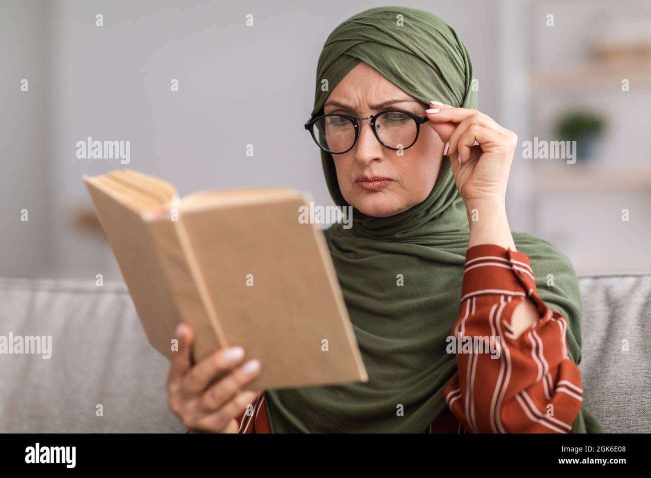 Senior Muslim Lady Squinting Eyes Reading Book Wearing Eyeglasses Indoor Stock Photo