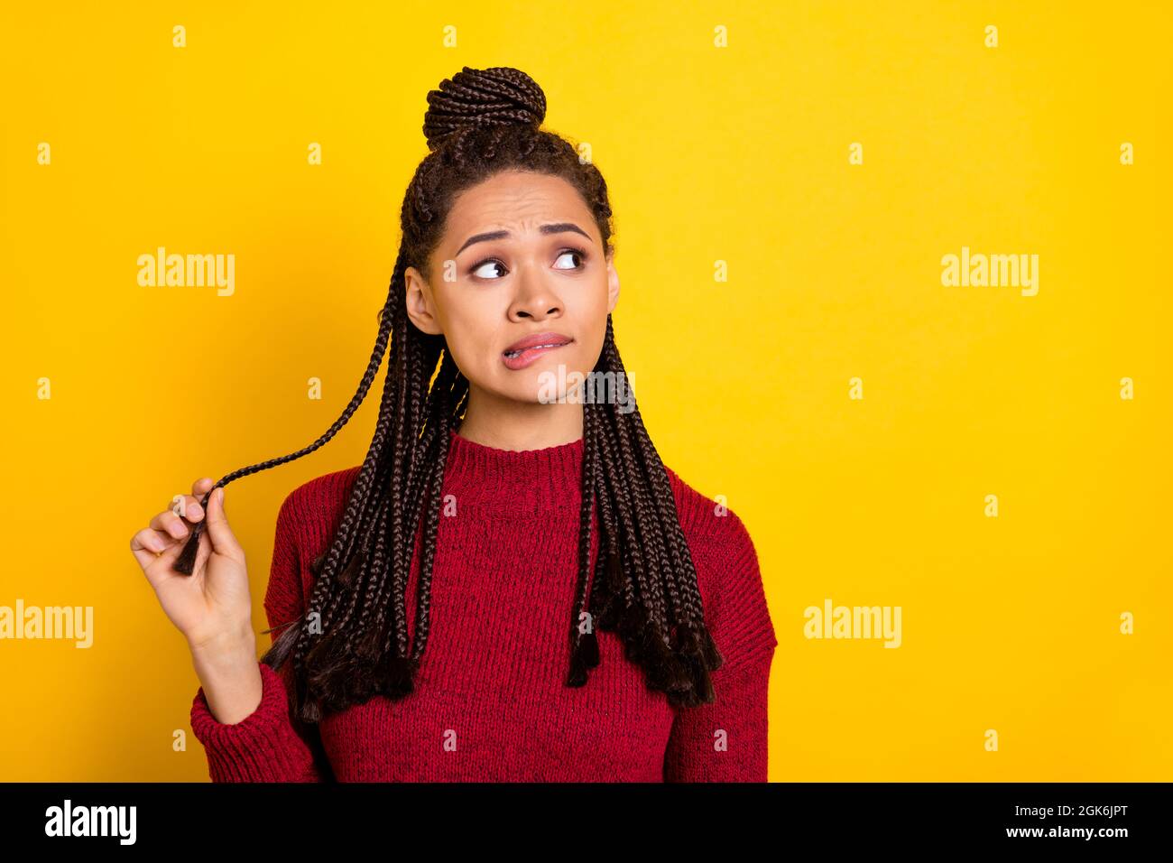 Photo of guilty doubtful dark skin woman dressed red sweater biting lip looking empty space isolated yellow color background Stock Photo