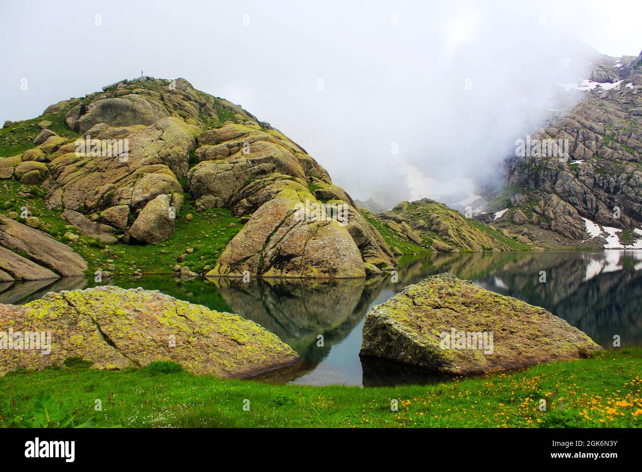Calm reflective lake with rocks and stones on the foggy background ...
