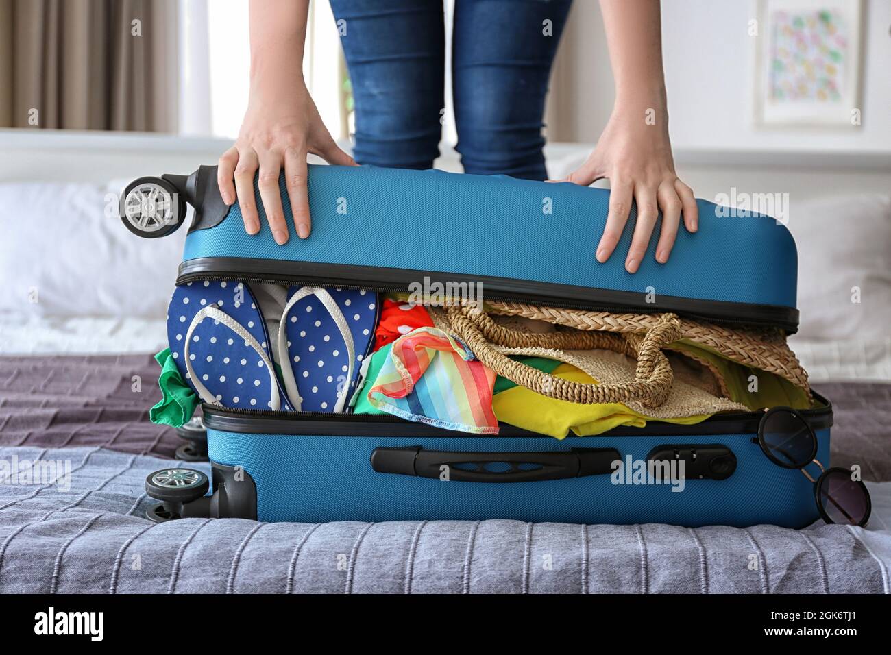 Woman trying to lock heavy suitcase on bed. Luggage overweight concept