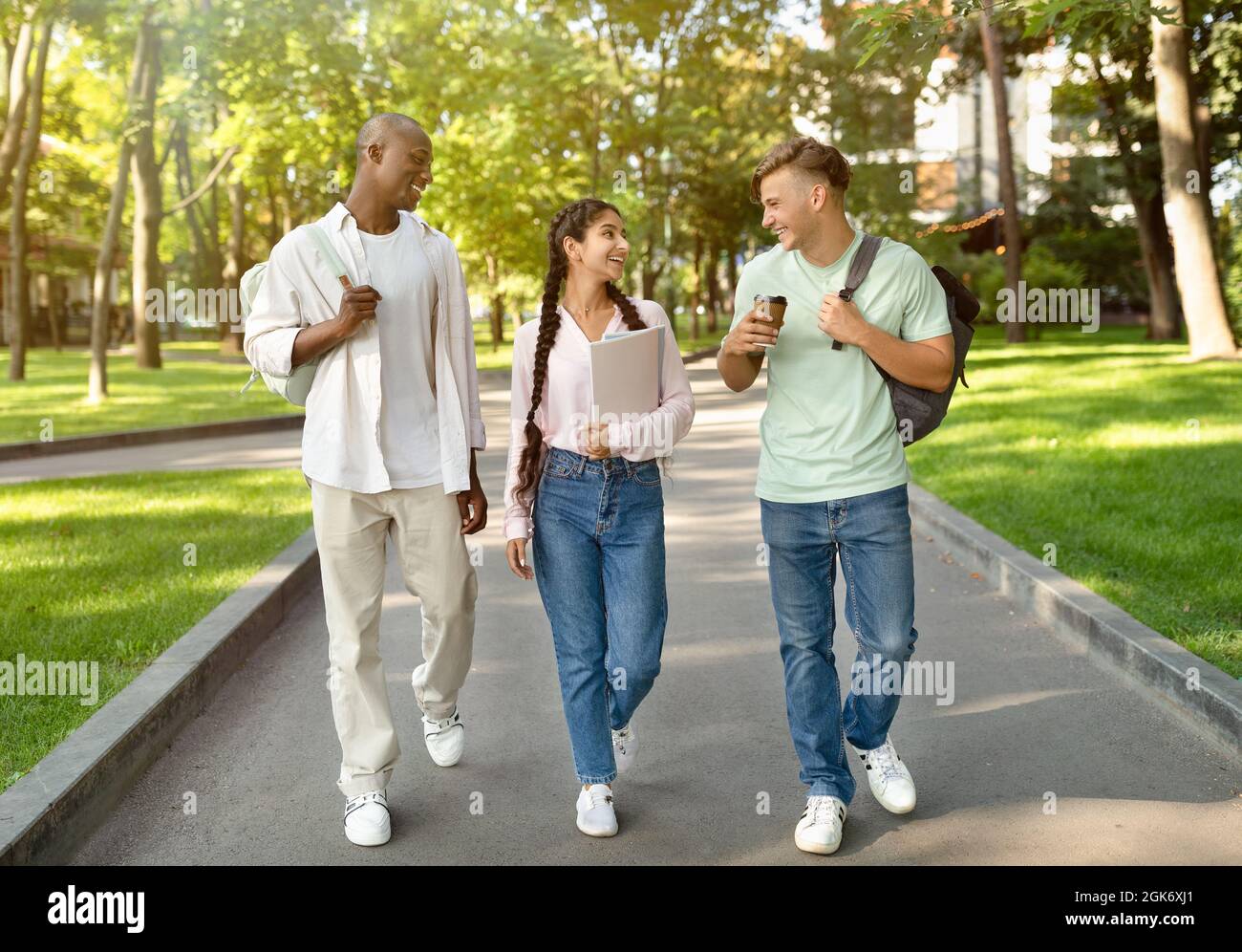 Three multiracial high-school students walking after study and talking ...