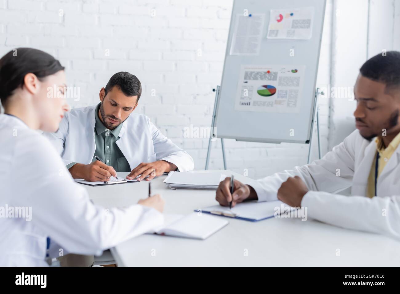 multicultural doctors writing in conference room near flip chart with ...