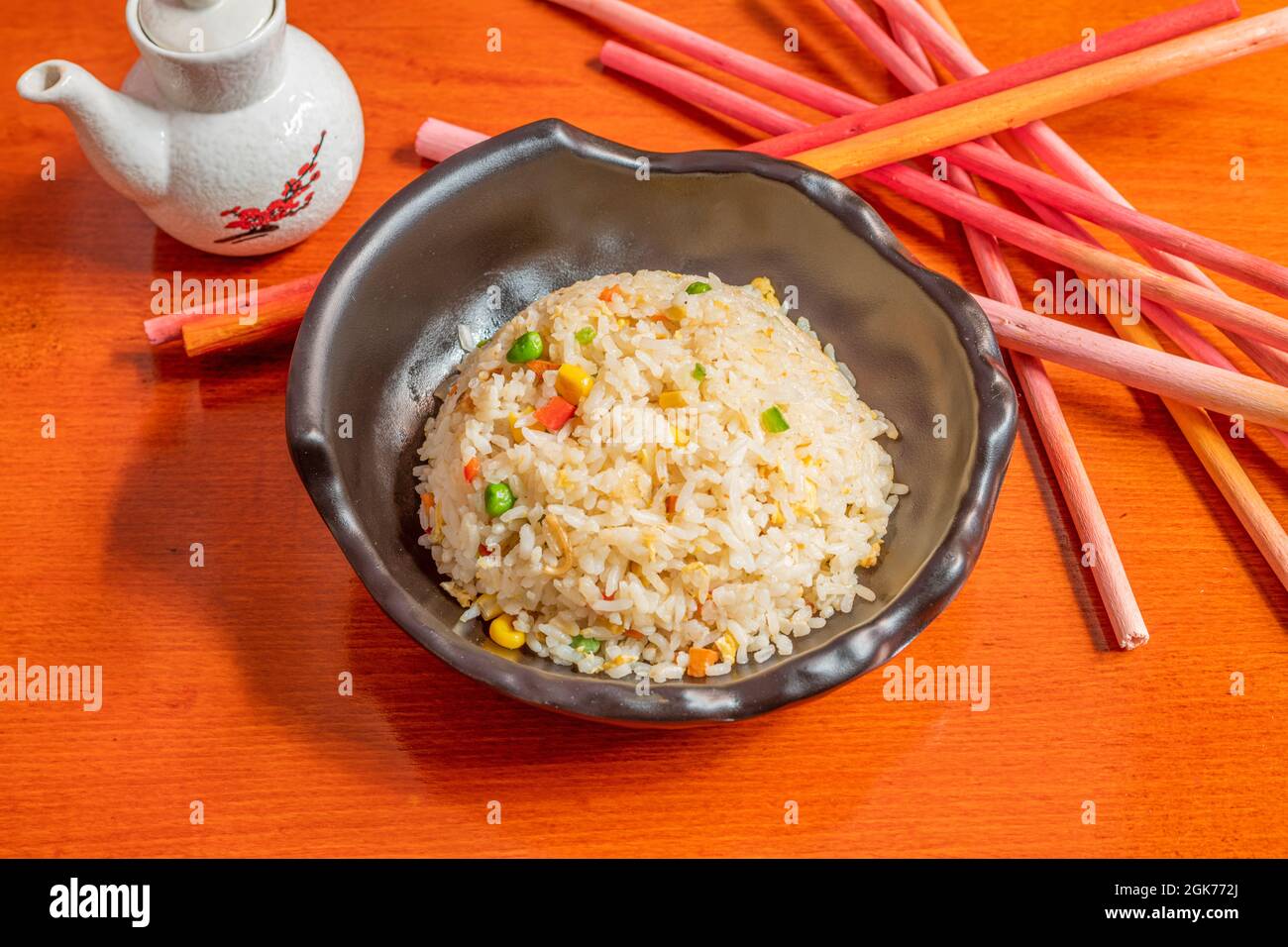 black bowl of fried rice with assorted vegetables, soy sauce in a jar