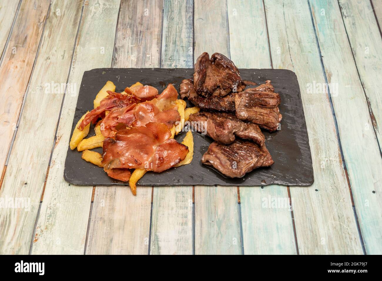 Grilled beef entrails fillets garnished with fried potatoes with fried ham on a black slate tray Stock Photo