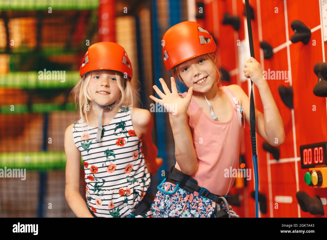 Indoor climbing class for kids. School girls smiling at the camera and having fun in indoor playground for children. Two happy little girls in red hel Stock Photo