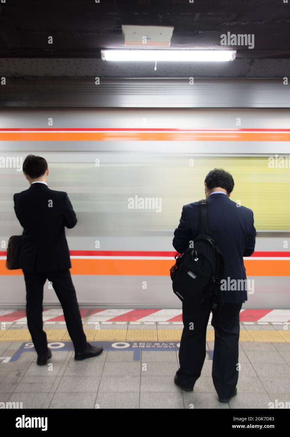 Communters stood on the platform as a metro train rushes in, Shinjuku station, Tokyo, Japan Stock Photo