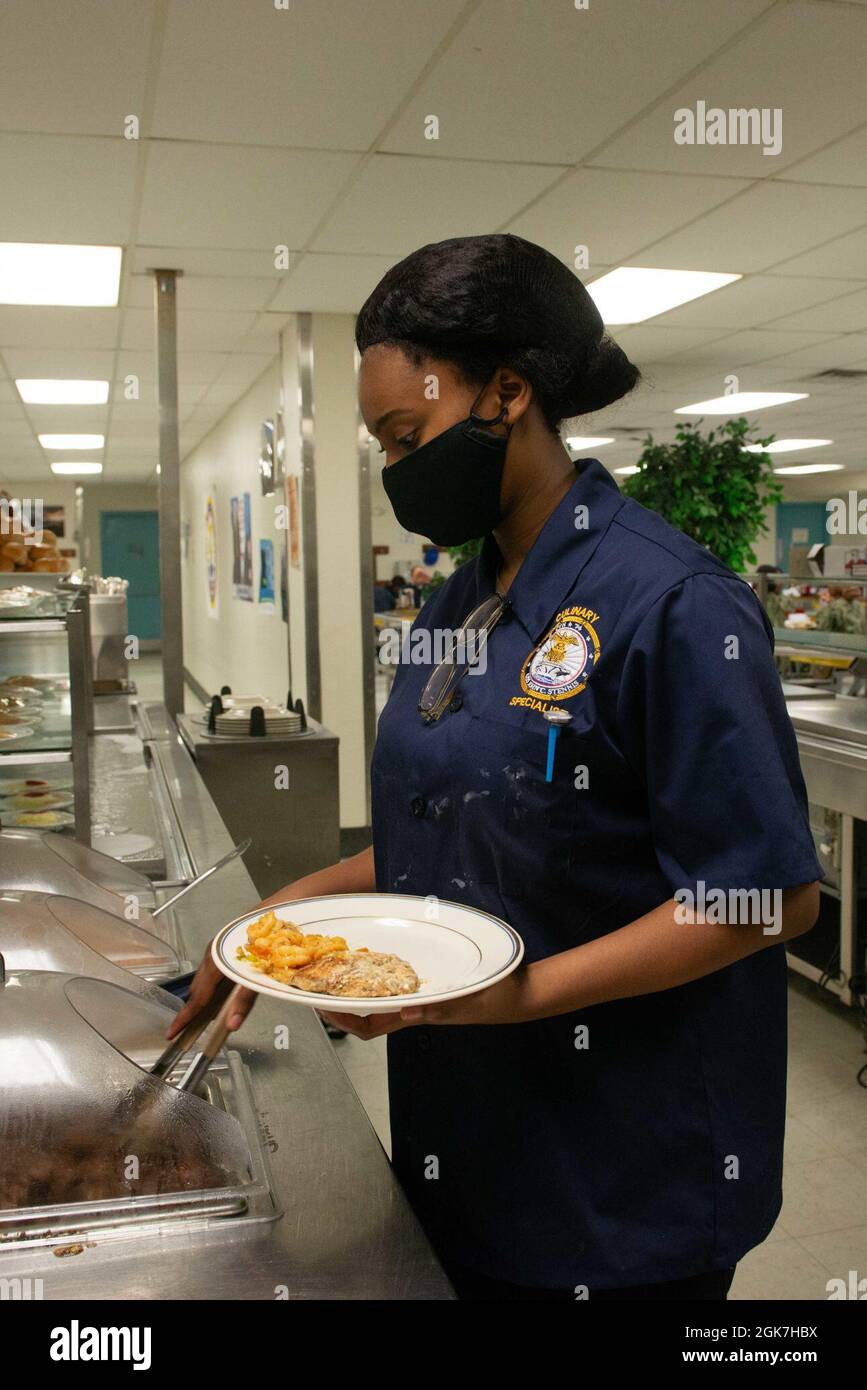 U.S. Navy Culinary Specialist Seaman Erica Lawson, from Tulsa, Oklahoma, assigned to the aircraft carrier USS John C. Stennis (CVN 74), serves the special Women’s Equality Day meal onboard the floating accommodation facility, in Newport News, Virginia, Aug. 26, 2021. John C. Stennis is in Newport News Shipyard working alongside NNS, NAVSEA and contractors conducting Refueling and Complex Overhaul as part of the mission to deliver the warship back in the fight, on time and on budget, to resume its duty of defending the United States. Stock Photo