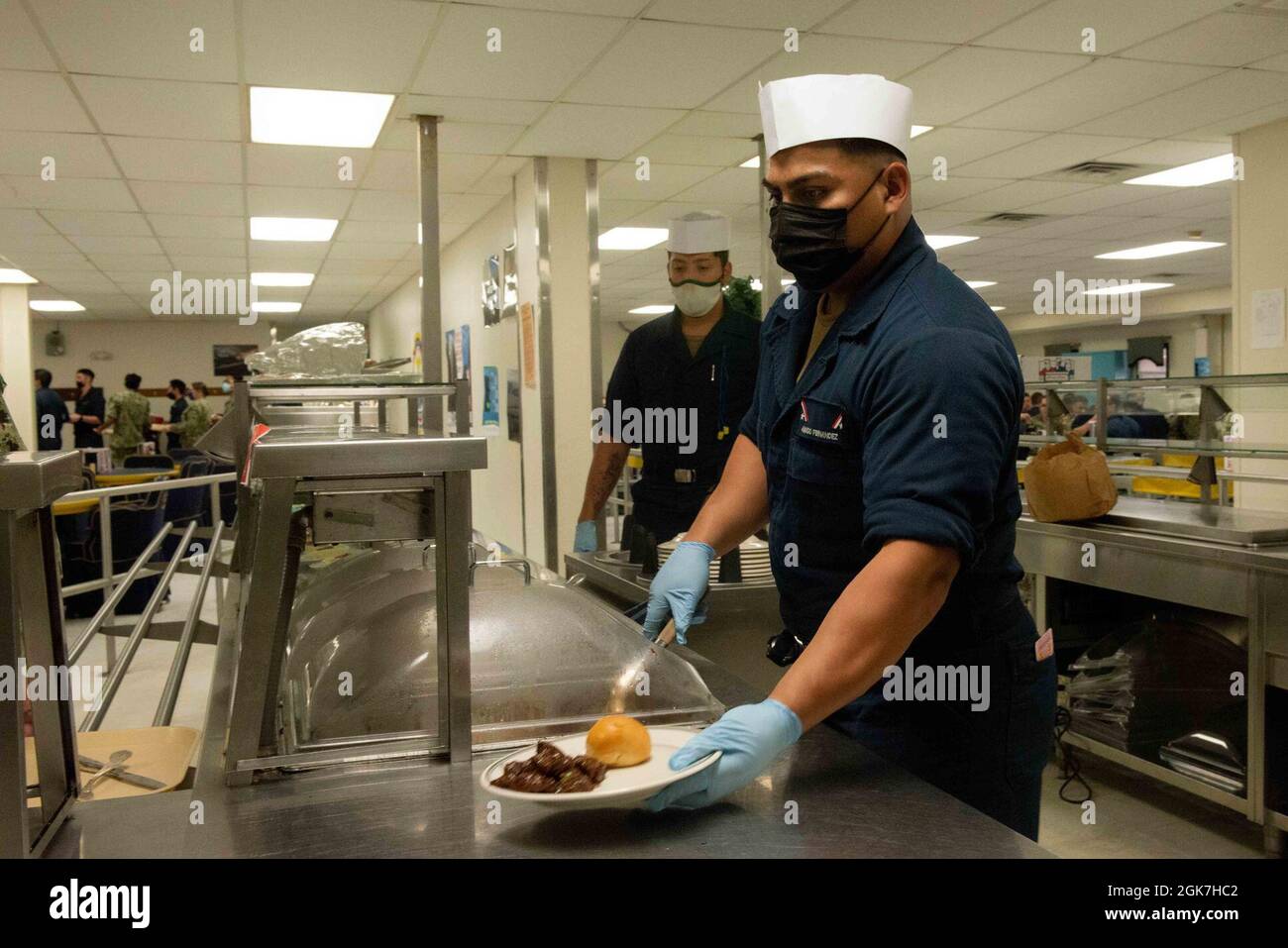 U.S. Navy Culinary Specialist Seaman Apprentice Amado Fernandez from Fresno, California, serves the special Women’s Equality Day meal on board the Floating Accommodation Facility attached to the aircraft carrier USS John C. Stennis (CVN 74), in Newport News, Virginia, Aug. 26, 2021. John C. Stennis is in Newport News Shipyard working alongside NNS, NAVSEA and contractors conducting Refueling and Complex Overhaul as part of the mission to deliver the warship back in the fight, on time and on budget, to resume its duty of defending the United States. Stock Photo
