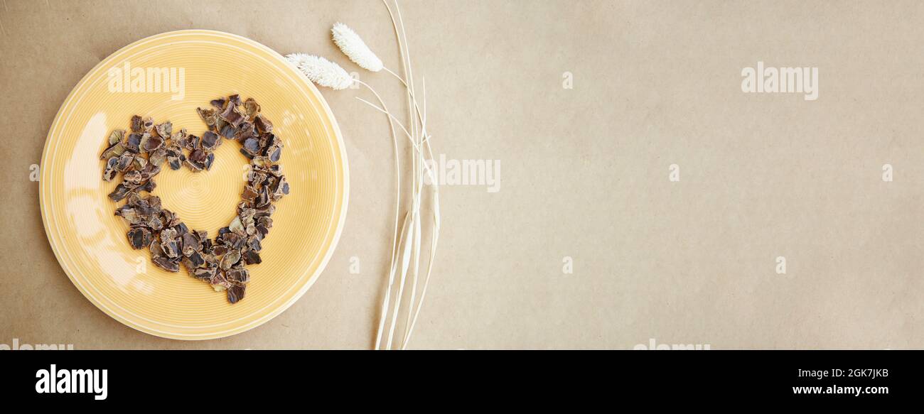Carob - plant-based alternative of coffee - natural product on the plate with dry Lagurus ovatus grass in the shape of heart. Organic antioxidants and Stock Photo