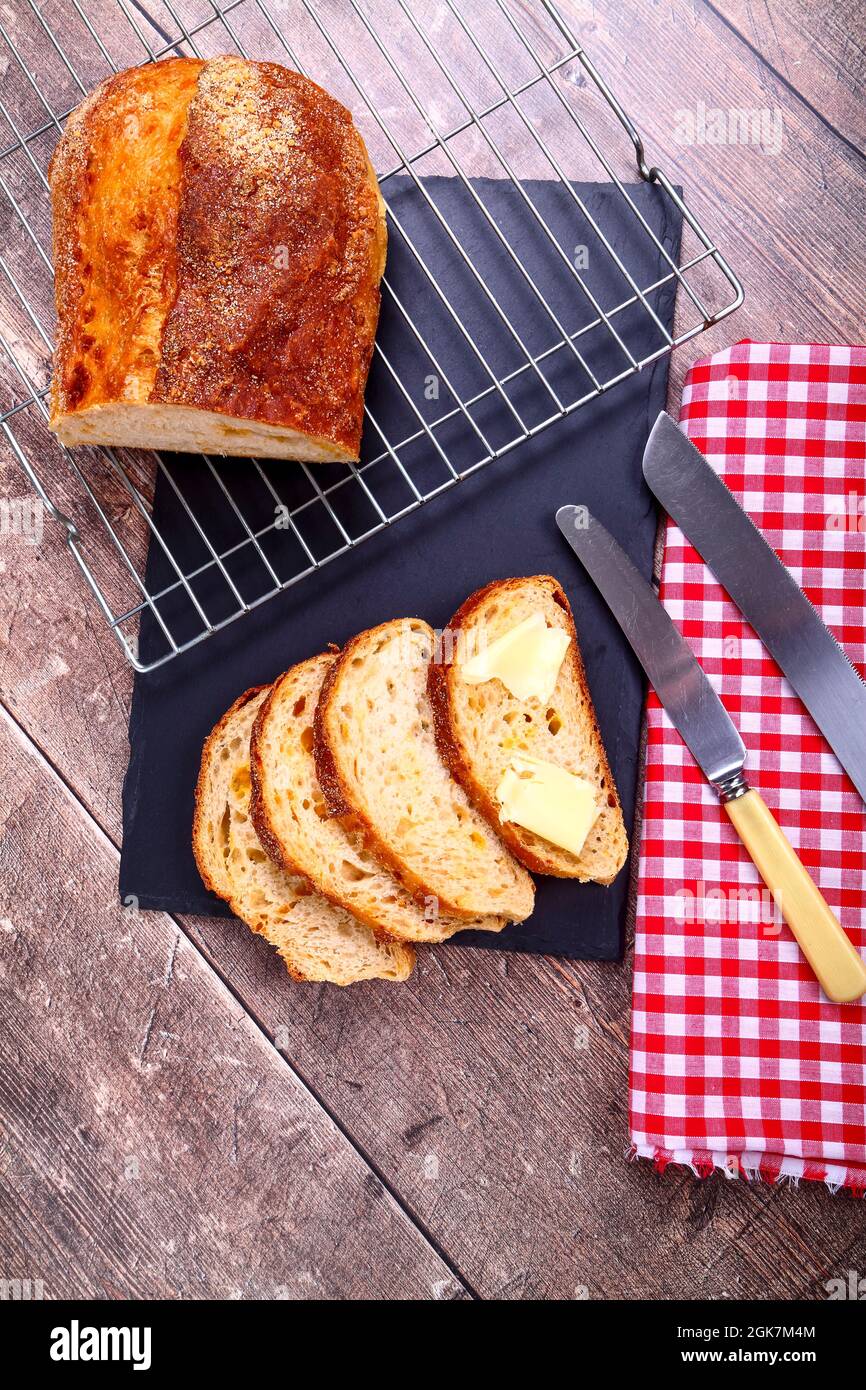 Freshly baked sourdough and cheese artisan bread laid on a wire metal cooling rack on a wooden table Stock Photo