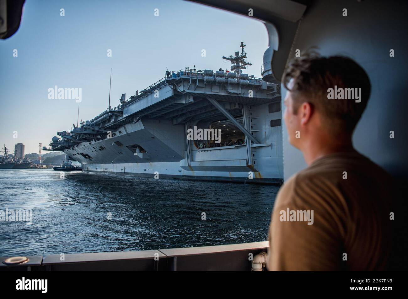 YOKOSUKA, Japan (Aug. 28, 2021) — Hull Maintenance Technician 1st Class Andrew Stewart, attached to Commander, Fleet Activities Yokosuka's (CFAY) port operations department, looks out from Yard Tug Seminole (YT-805) at the Nimitz-class aircraft carrier, USS Carl Vinson (CVN 70) while it enters Berth 12 for a scheduled port visit. Carl Vinson, homeported in San Diego, Calif., and the accompanying Carrier Strike Group (CSG 1), are on a rotational deployment in the U.S. 7th Fleet area of operations to enhance interoperability with partners and serve as a ready-response force in support of a free Stock Photo