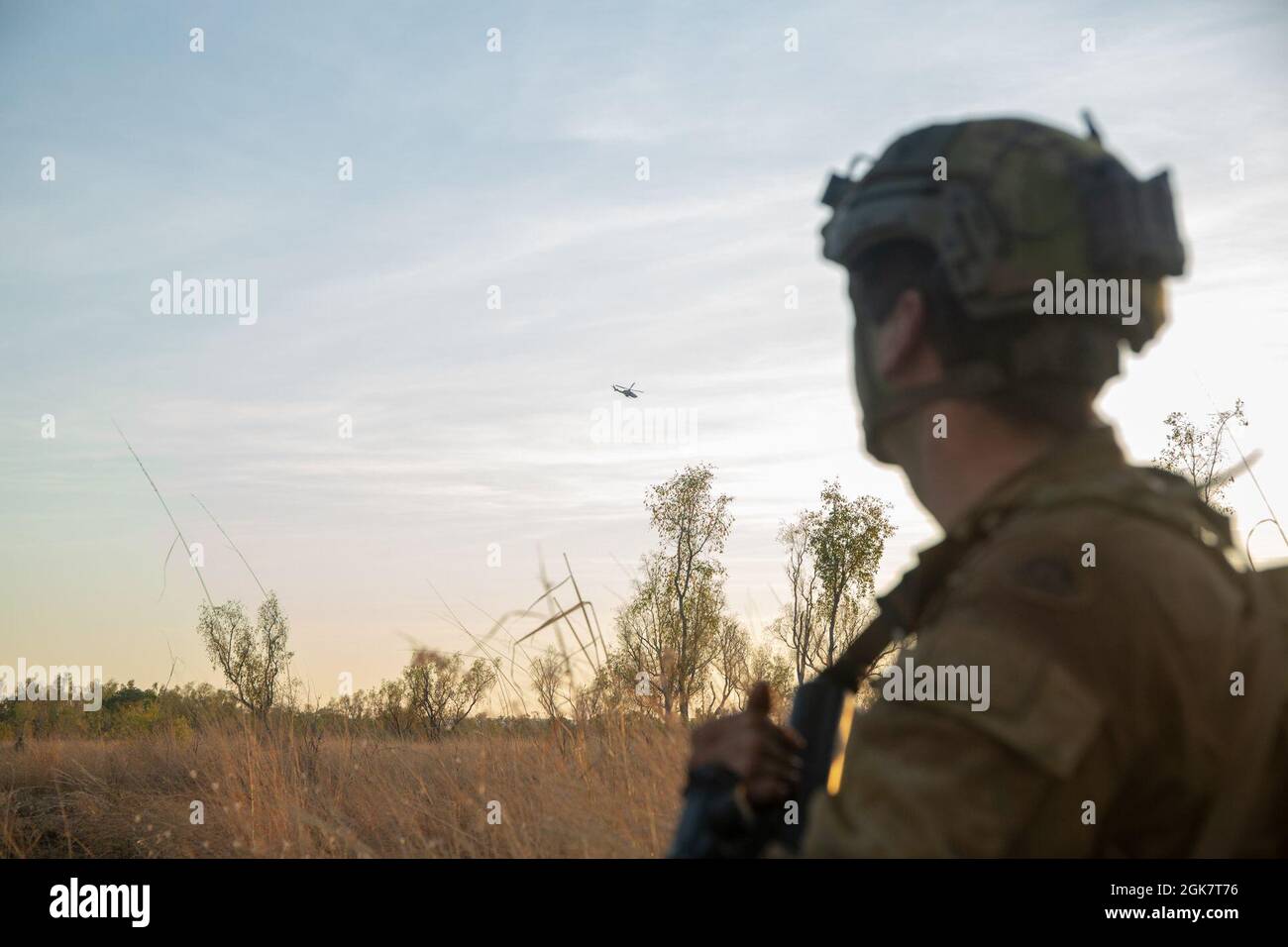 An Australian Army soldier looks on as an AH-1Z Viper makes a reconnaissance pass over the objective during Exercise Koolendong at Bradshaw Field Training Area, NT, Australia, Aug. 29, 2021. Australian Defence Force Members worked with U.S. Marines to conduct an aerial assault simulation. Exercise Koolendong validates Marine Rotational Force - Darwin and the Australian Defence Force’s ability to conduct expeditionary command and control operations, demonstrating the shared commitment to being ready to respond to a crisis or contingency in the Indo-Pacific region. Stock Photo