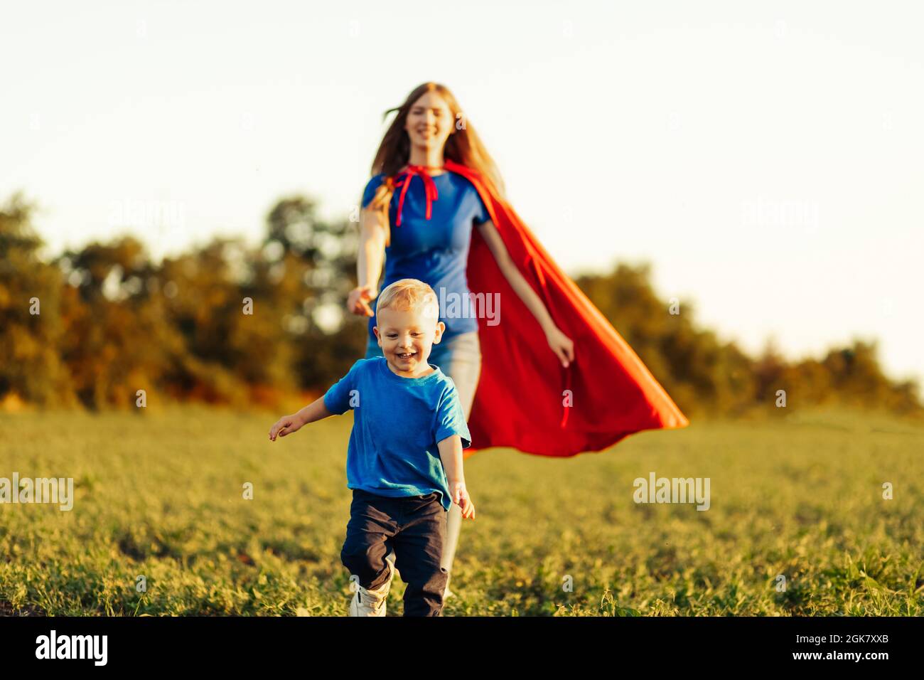 concept of super mom with baby, mom with super hero cloak runs after baby, outdoors, in nature at sunset Stock Photo