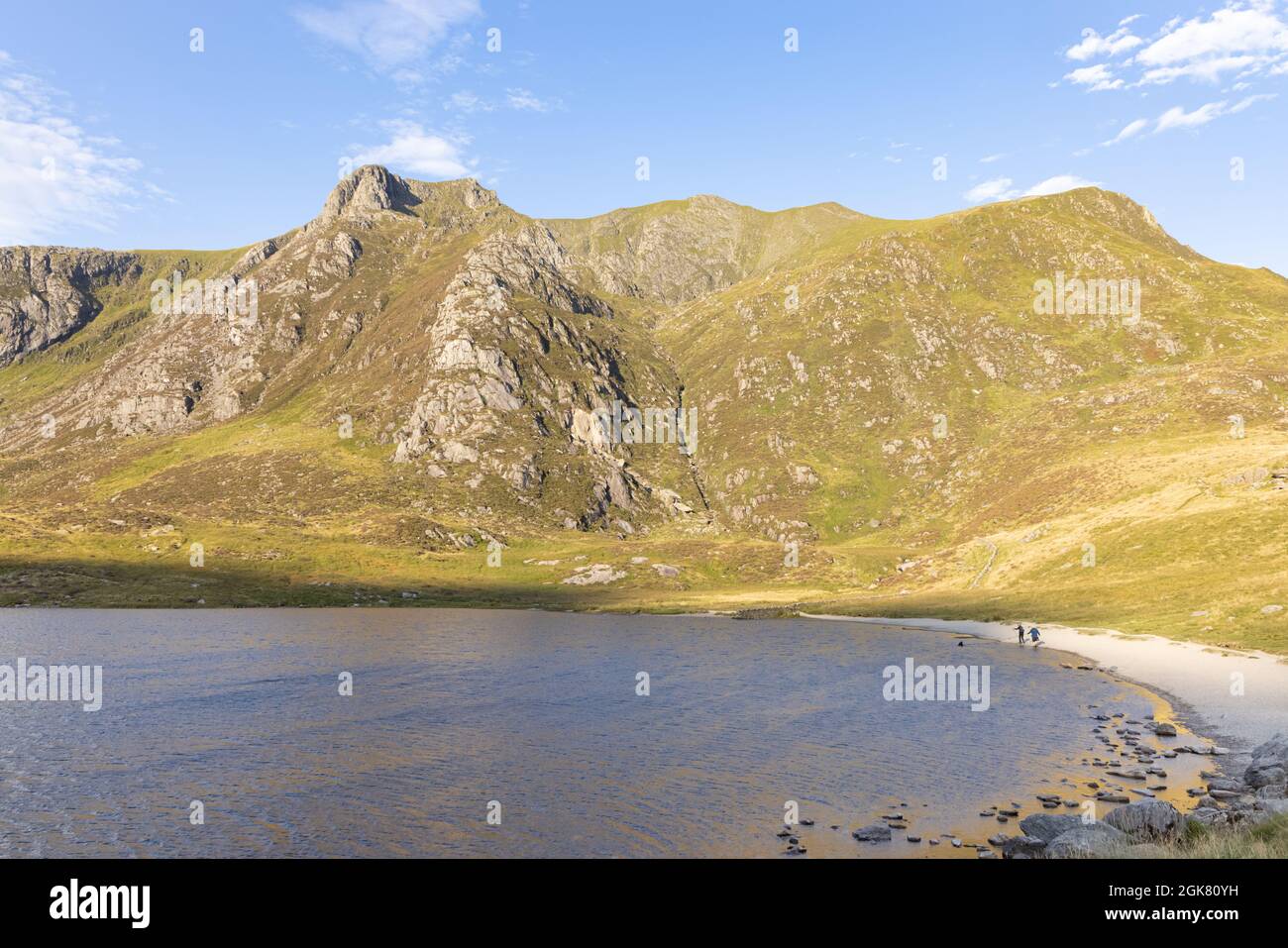 Llyn Idwal, Snowdonia, UK, September 8th 2021: Two people walking along the shingle beach of Llyn Idwal with the crags of Castell y Geifr behind. Stock Photo