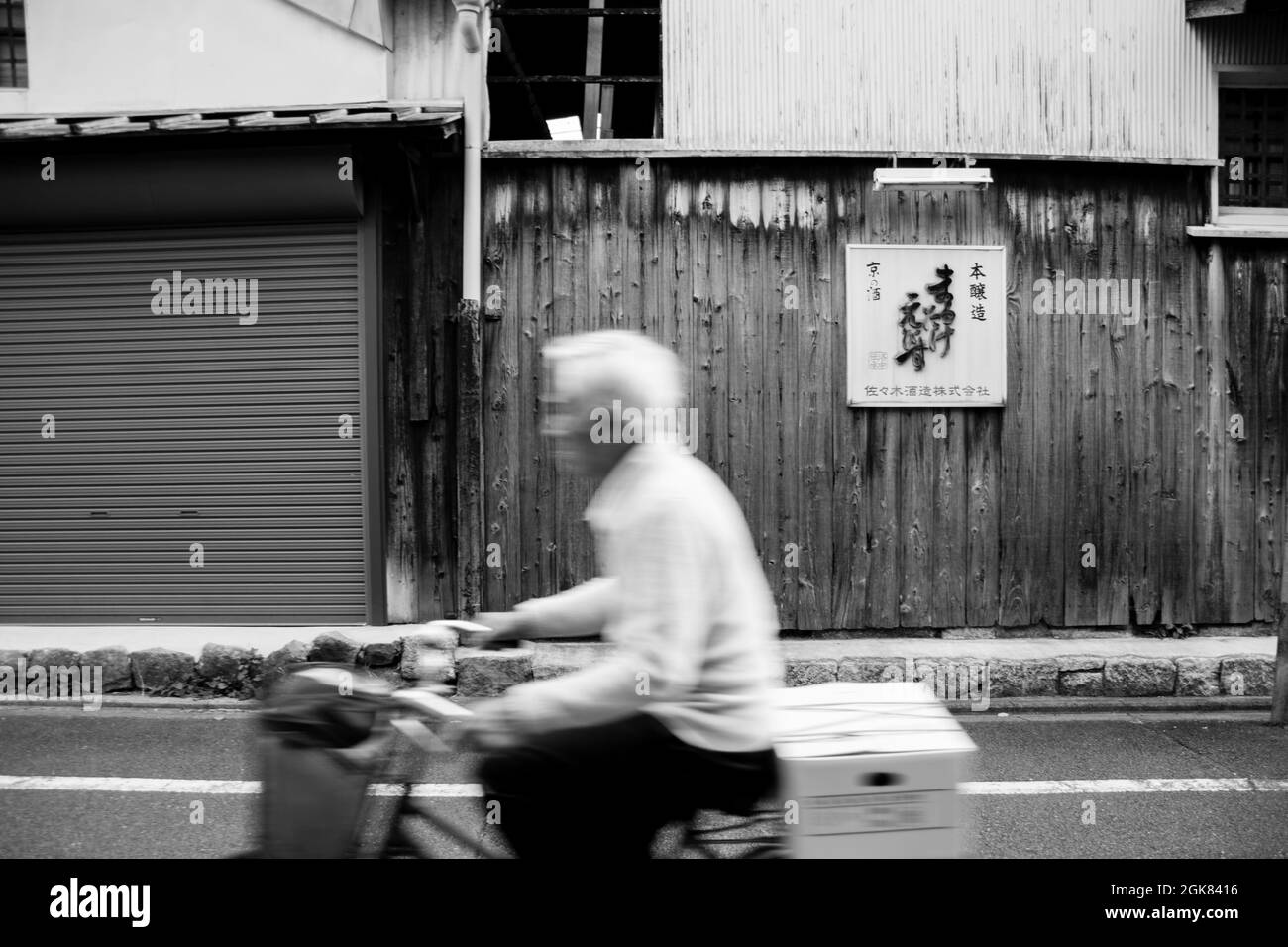 Elderly male Japanese cyclist cycling down side street in Kyoto, Japan Stock Photo