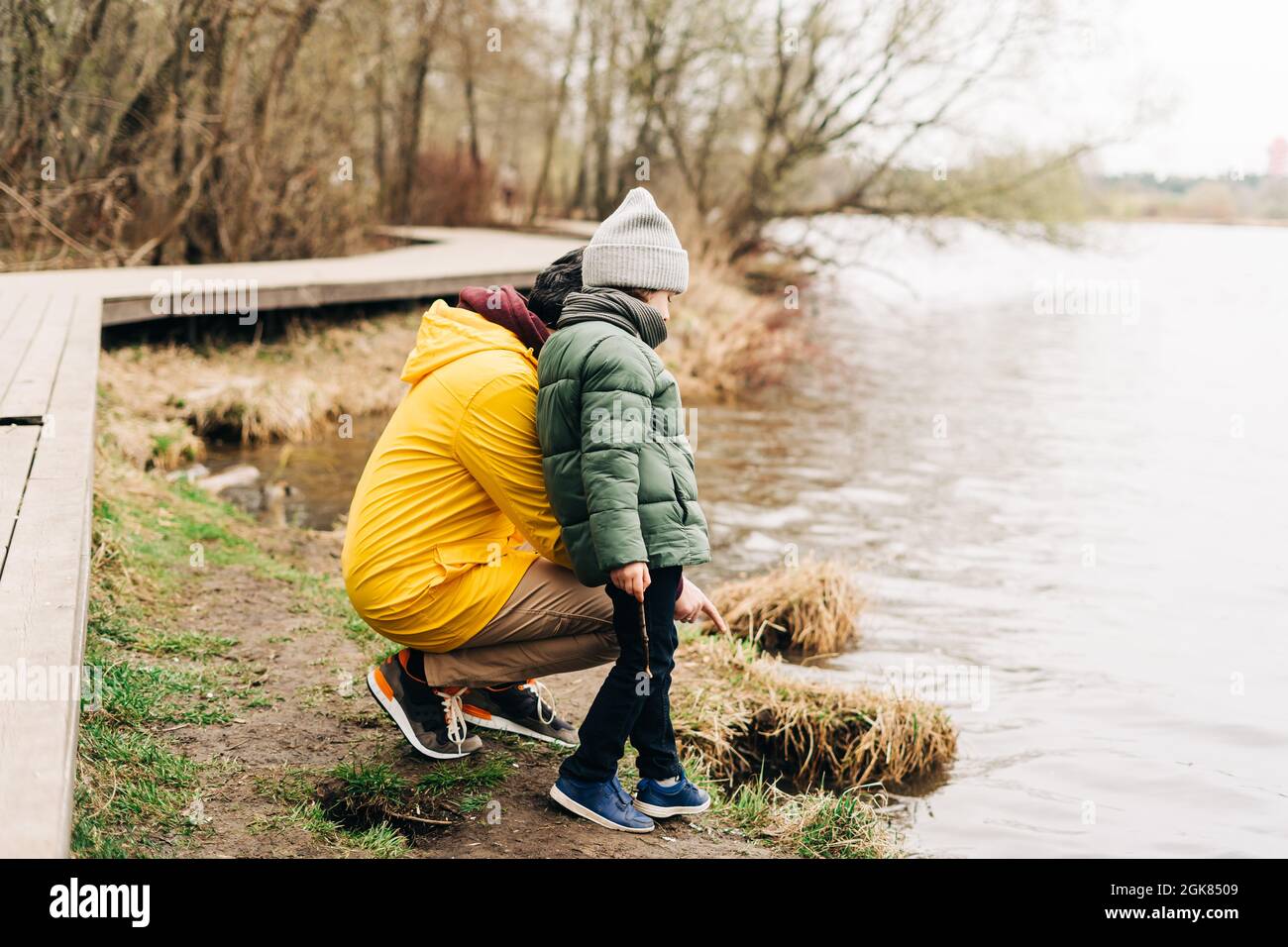 Father and son stand on the shore of the lake and playing with water. Happy family with child kid boy playing and having fun outdoors over autumn park Stock Photo