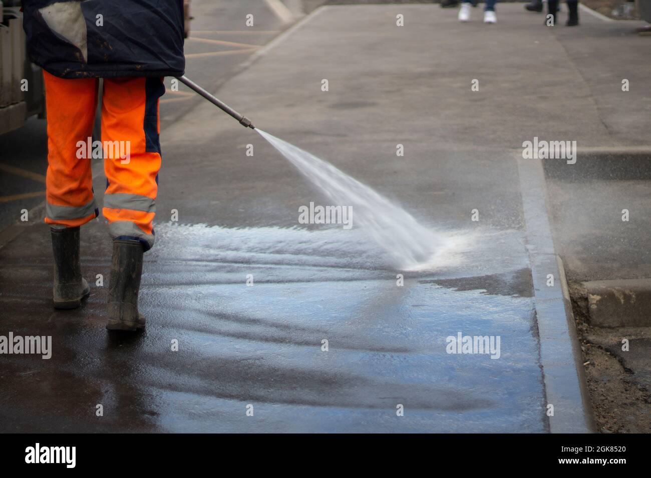 Cleaning up the public place. A jet of water washes the asphalt. Disinfection of the bus stop. Cleaning up the area. Laundering dirt. Stock Photo