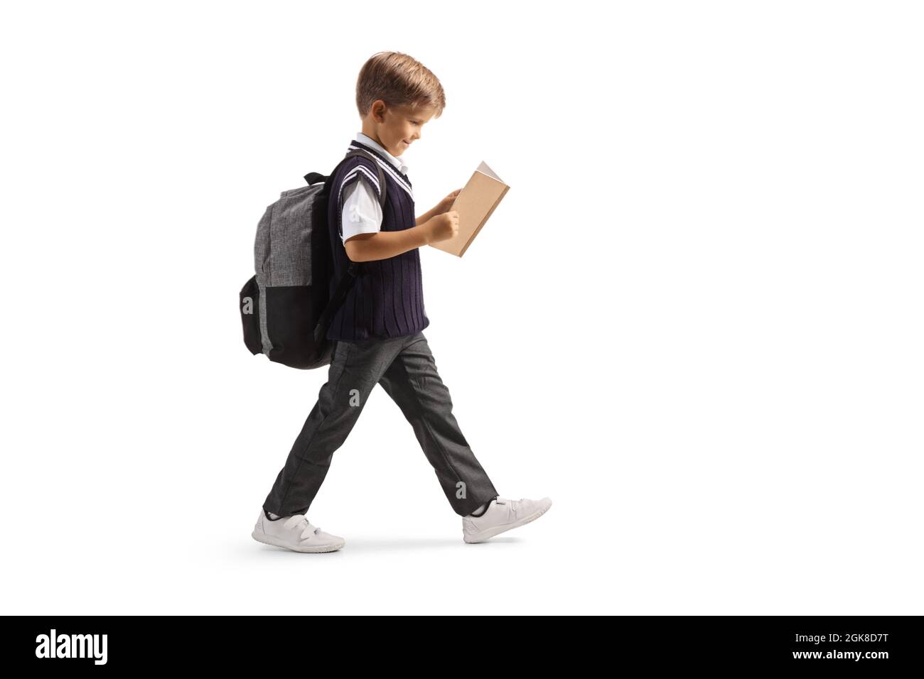 Full length profile shot of a schoolboy in a uniform walking and reading a book isolated on white background Stock Photo