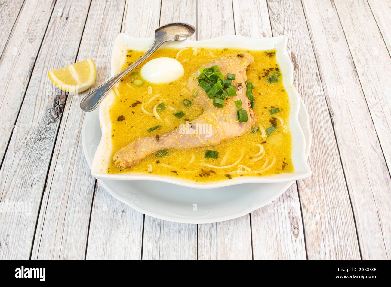 Typical Peruvian chicken broth with old chicken leg, assorted vegetables, noodles, boiled egg and a lot of boiling liquid on a light table Stock Photo