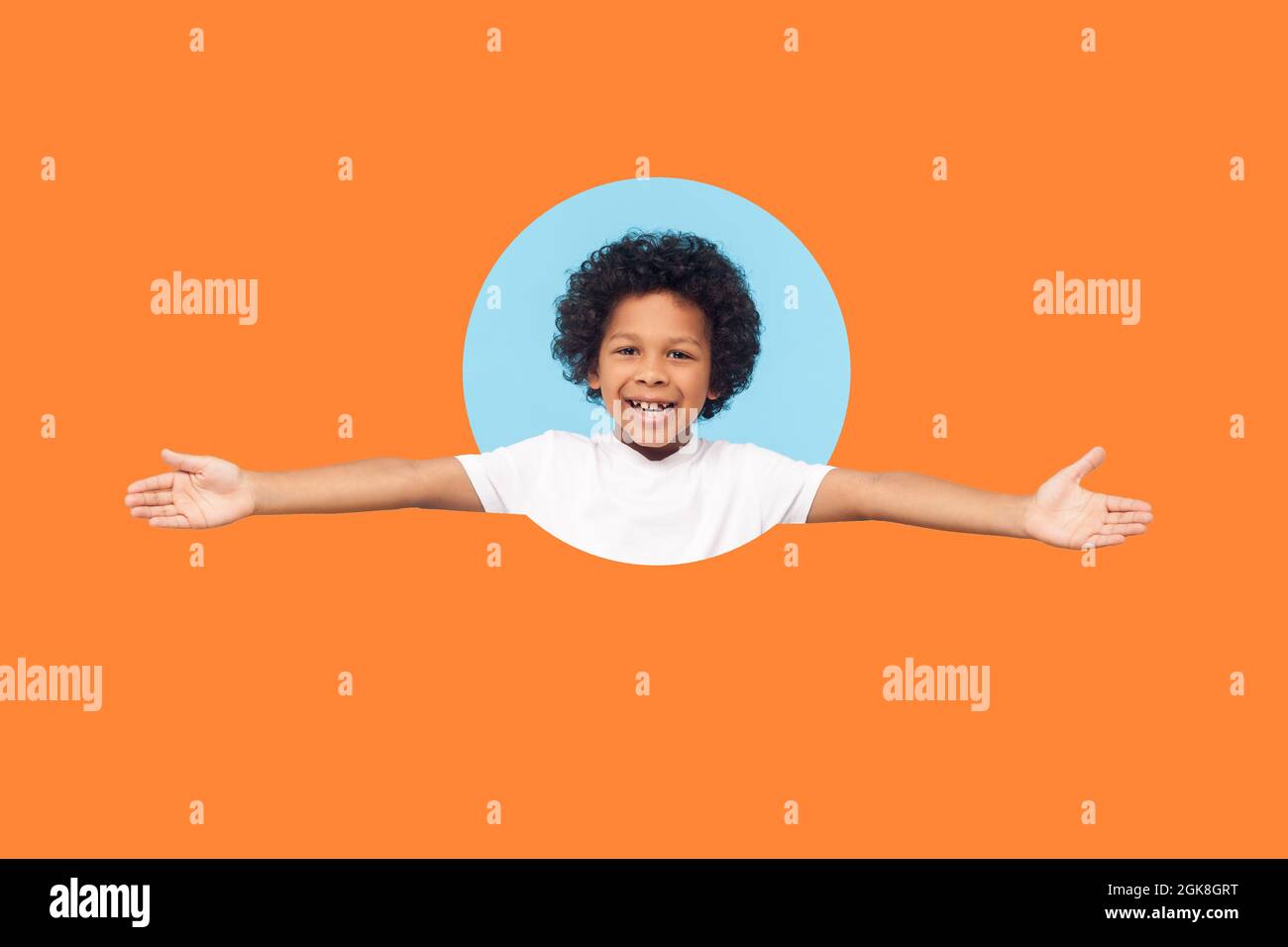 Let's hug. Portrait of friendly little boy with curls in white T-shirt smiling happily and holding hands wide open to embrace, welcome. indoor shot is Stock Photo