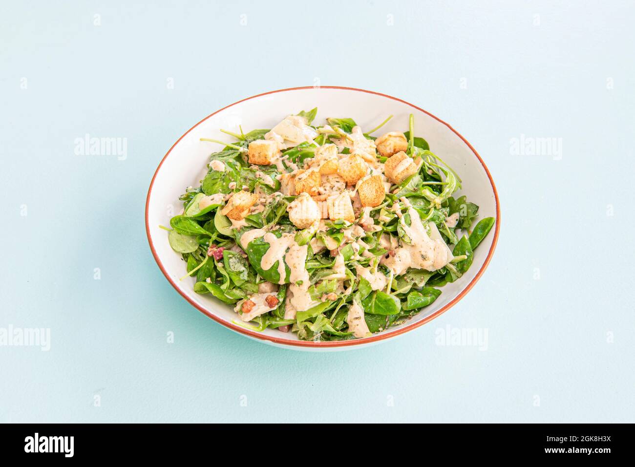 Bowl of caesar salad with lamb's lettuce, croutons, dried fruits and mayonnaise on blue background Stock Photo