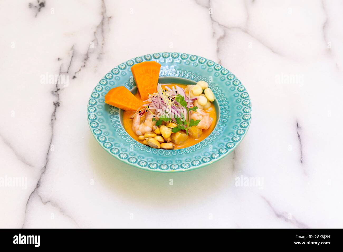 Mixed sea bass and prawn ceviche with marinated sweet potato and corn on a blue deep plate on a marble table Stock Photo