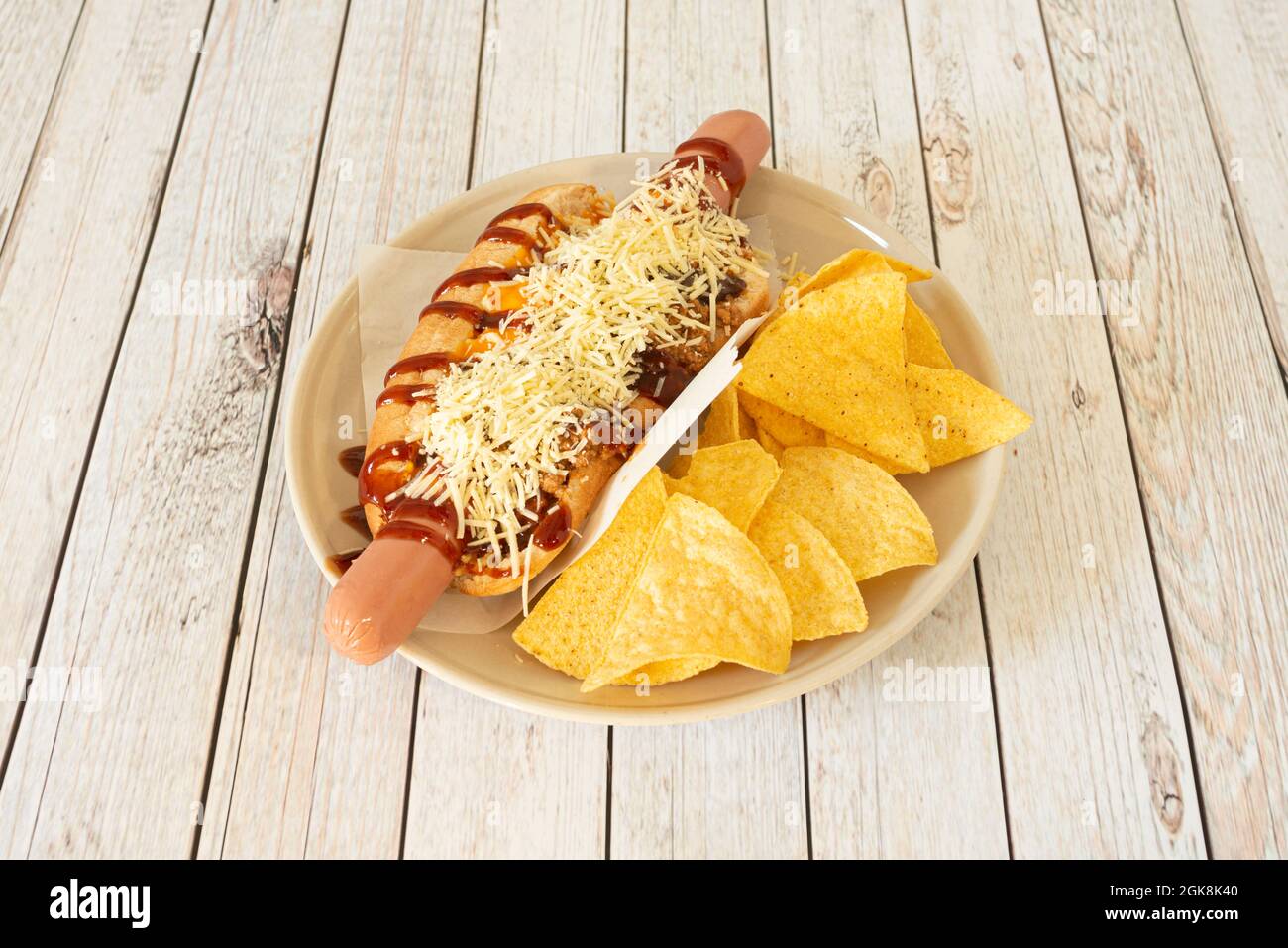 Spicy hot dog with chili, barbecue sauce, grated cheese and corn chips Stock Photo
