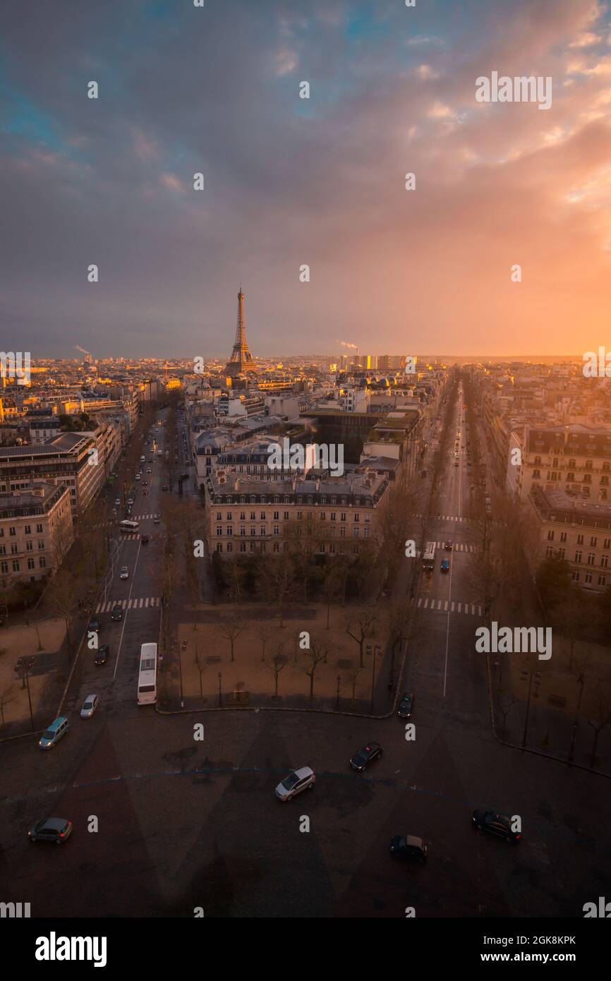 Drone view of urban house facades and roadways with transport under shiny cloudy sky at sundown