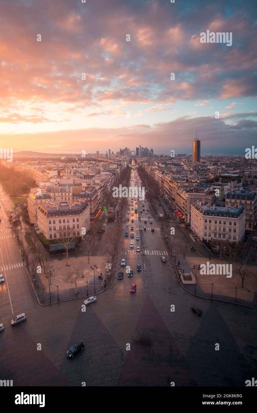 Drone view of urban house facades and roadways with transport under shiny cloudy sky at sundown