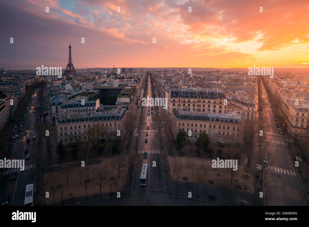 Drone view of urban house facades and roadways with transport under shiny cloudy sky at sundown