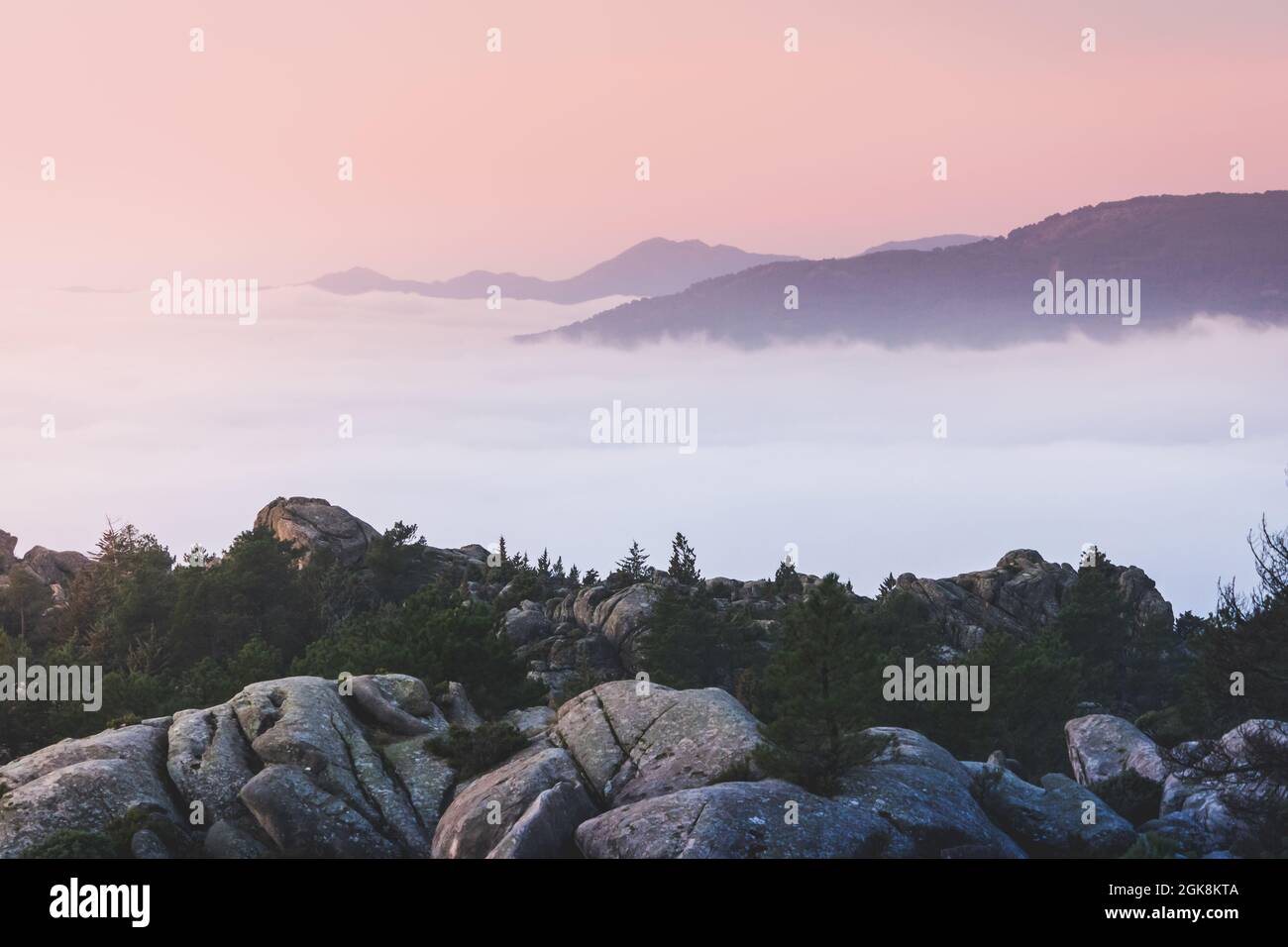 Scenic view of Pedriza with mist diffusing between Guadarrama mountain range and boulders with coniferous trees at sunrise in Spain Stock Photo