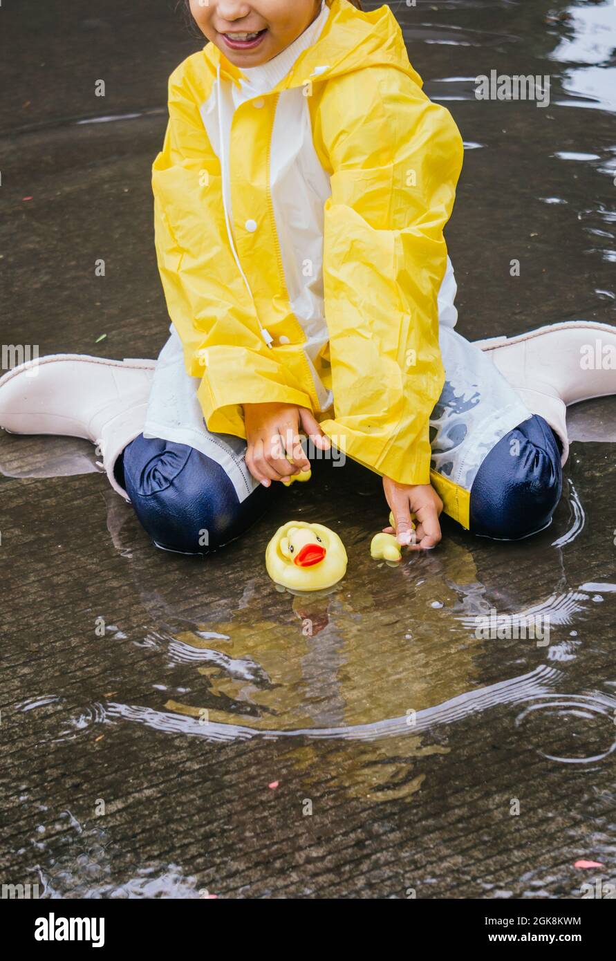 Crop kid in raincoat playing with plastic ducks reflecting in rippled  puddle in rainy weather Stock Photo - Alamy