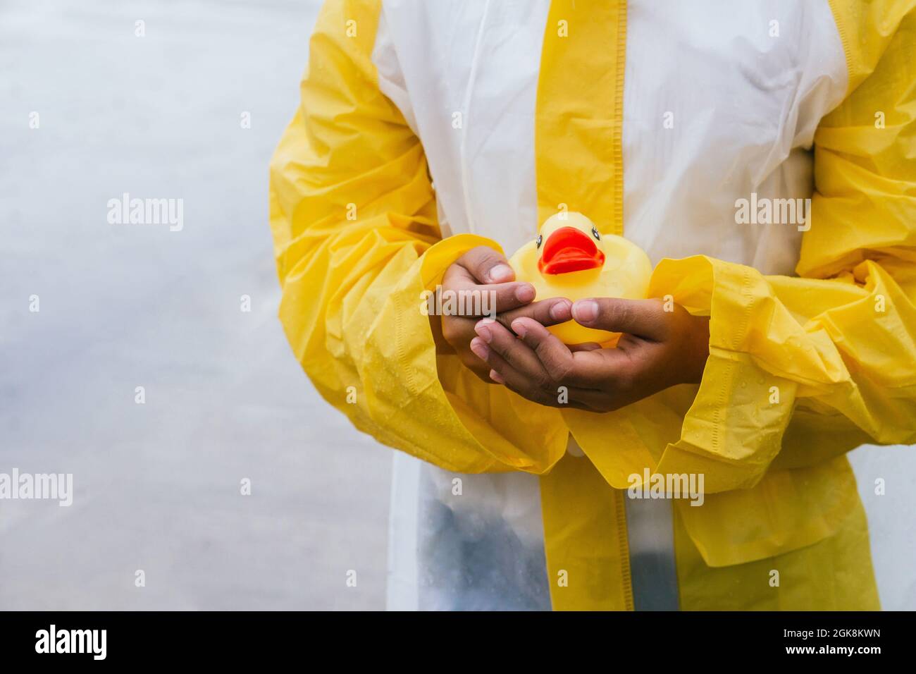 Crop kid in slicker with wet hair and rubber duck on grey background Stock Photo