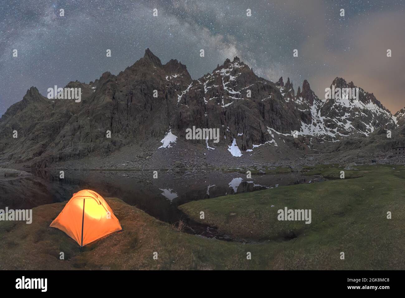 Scenic view of tent on lake shore against snowy mountain under cloudy sky in evening Stock Photo