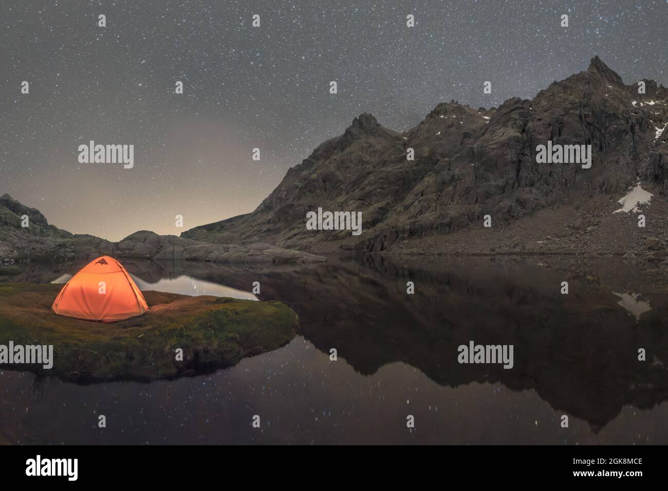 Scenic view of tent on lake shore against snowy mountain under cloudy sky in evening Stock Photo
