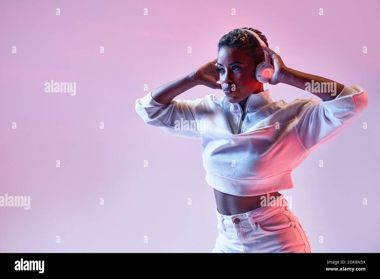 Energetic ethnic Woman in wireless headphones and trendy clothes dancing hip hop looking away Stock Photo