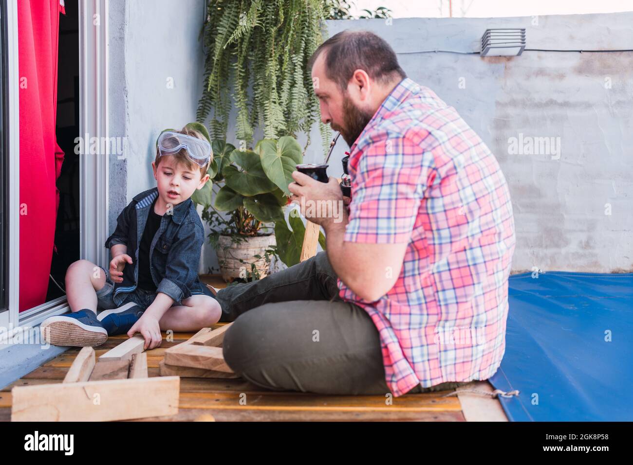 https://c8.alamy.com/comp/2GK8P58/hipster-dad-drinking-herbal-tea-from-calabash-gourd-against-son-working-with-wood-2GK8P58.jpg