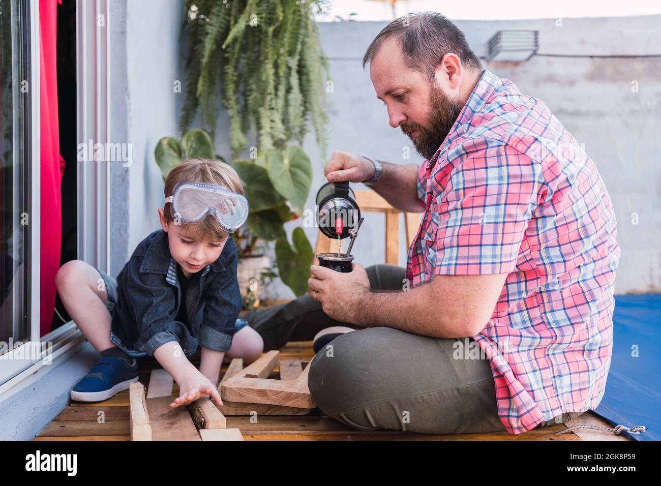 Hipster dad pouring herbal tea from thermos into calabash gourd against boy  with lumber on boardwalk Stock Photo - Alamy