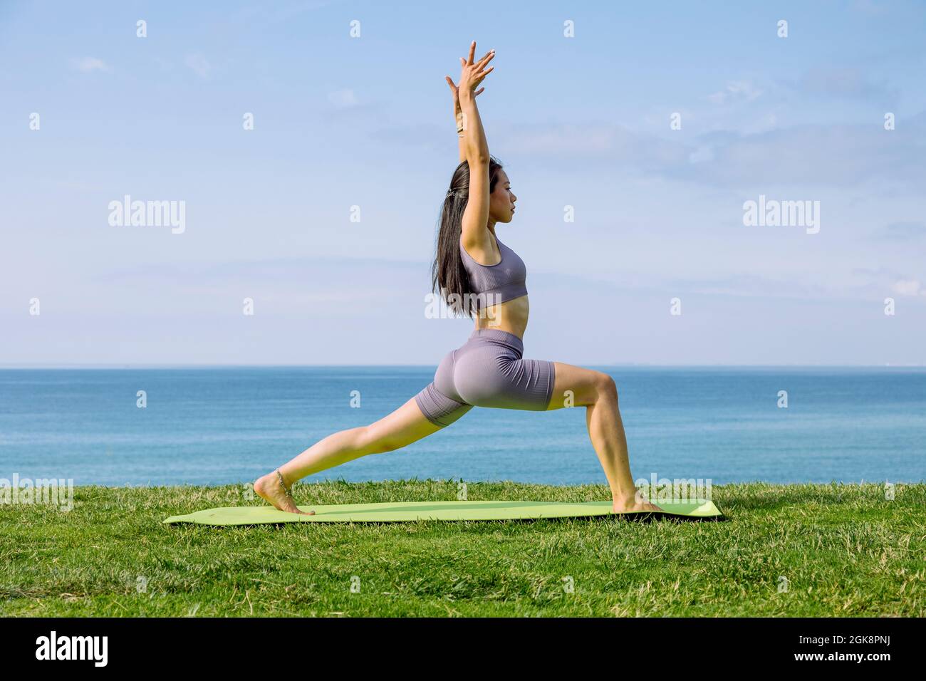 Side view of young ethnic female in sportswear standing in Ashta Chandrasana pose during yoga practice on sea shore Stock Photo