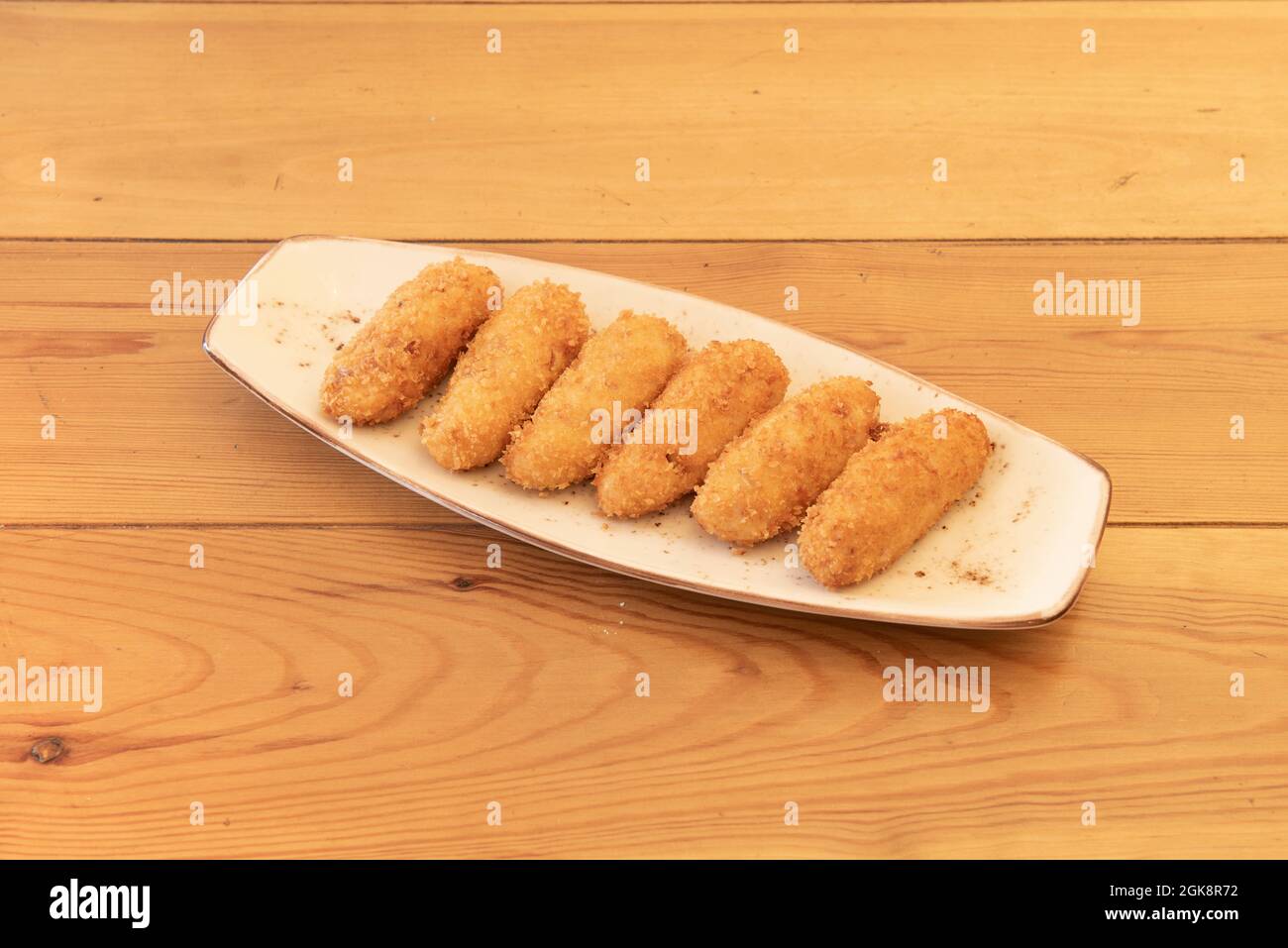 delicious Spanish tapa of homemade croquettes breaded and stuffed with cream with Iberian ham on wooden table Stock Photo